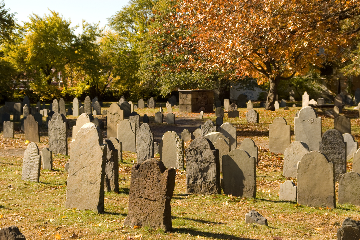 Headstones in a cemetery, leaning to various angles, showing their age.