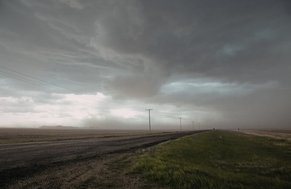 View of tornado brewing over an empty plot of farm land and a road
