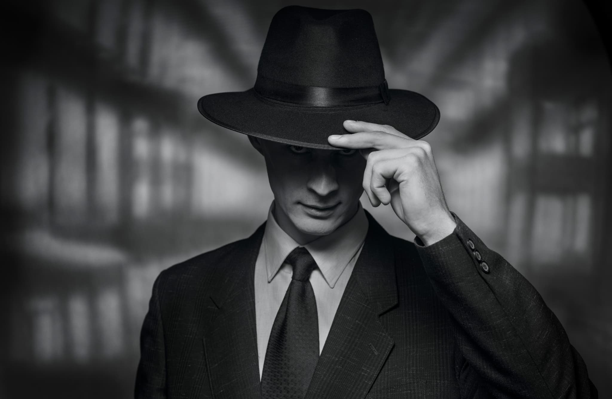 Close-up of a man in a suit and fedora tipping his hat, in black and white.