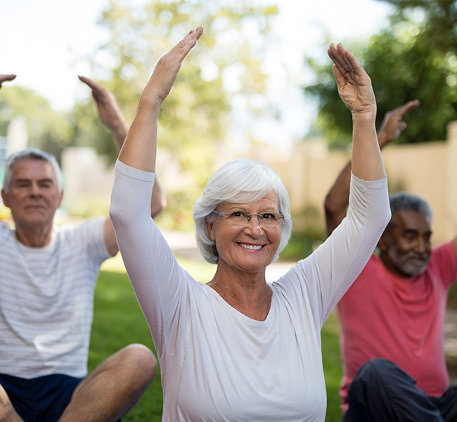 Senior woman doing a seated stretch outdoors during yoga class